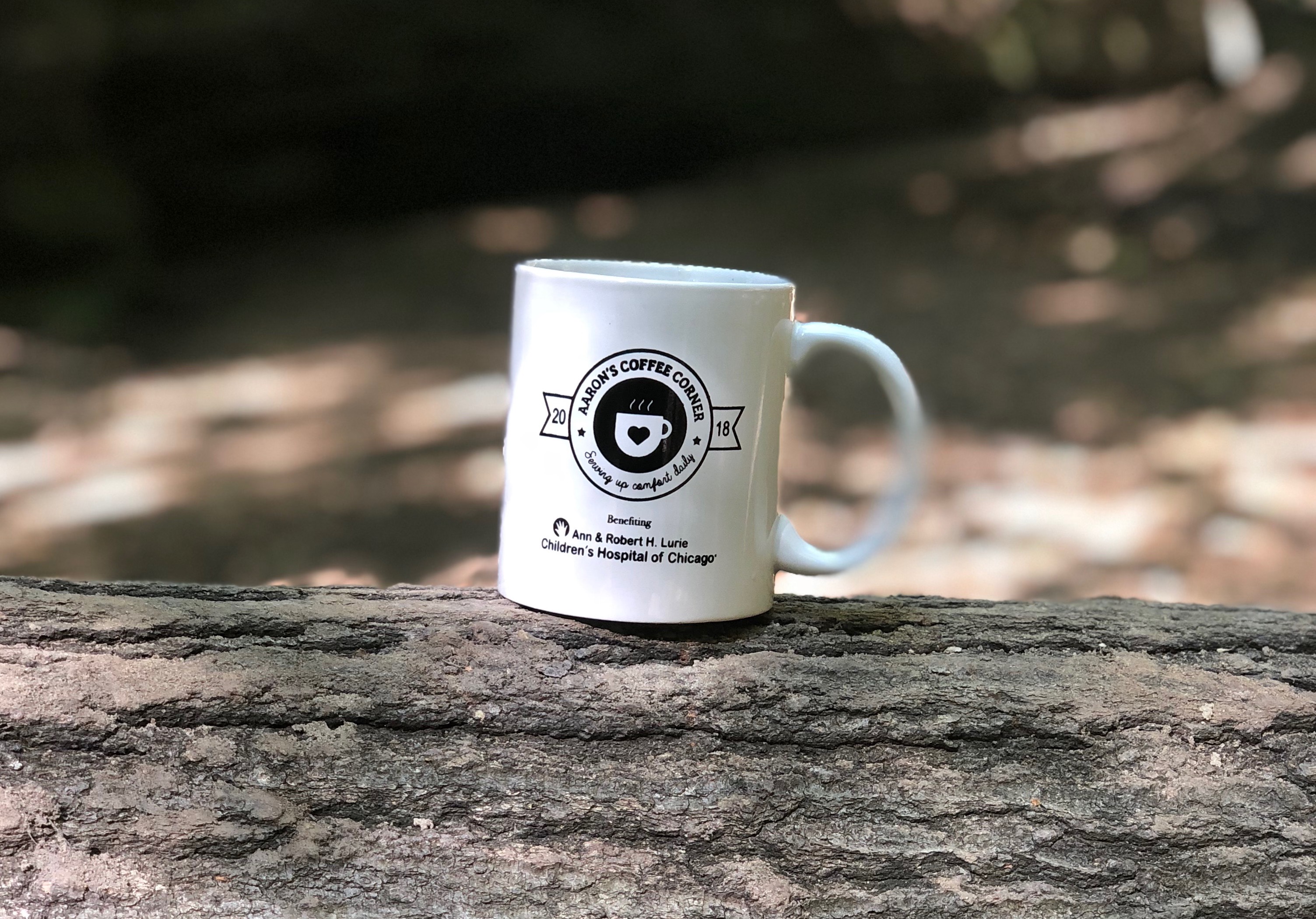 Background photo of an Aaron's Coffee Corner mug on a log in nature